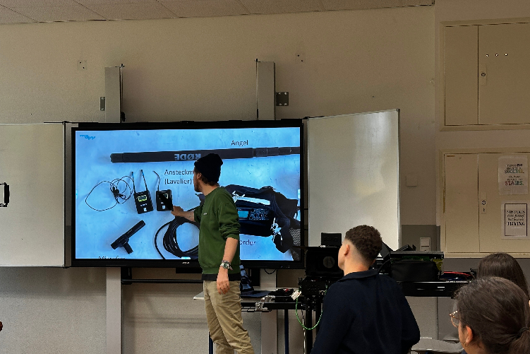 Ein Teil der Technik Crew erklärt den Jugendlichen an einem White Board in einem Klassenzimmer über eine Präsentation die wichtigsten Infos zum Film-Equipment.