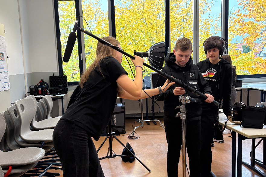 Eine Mitarbeiterin der MAPP Media GmbH zeigt zwei Schülern, wie sie den Mikrofonarm richtig einstellen.