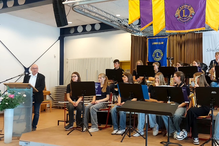 Programmleiter Dr. Peter Sicking hinter dem Rednerpult, an seiner Seite ein Schulorchester des Schulzentrums Kühlungsborn