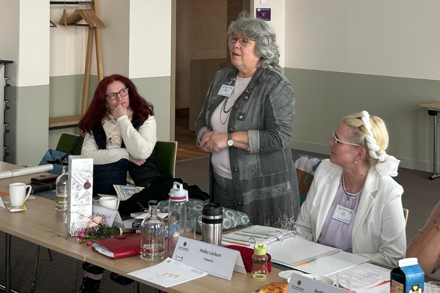 Auf dem Bild sind drei Lions-Quest Trainerinnen zu sehen. Kathrin Oppitz (Bildmitte) richtet ihr Wort an das Plenum